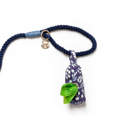 Fabric pouch dog poop bag holder attached to rope leash with snap closure loop to handle of rope dog leash in indigo background with multi-color foliage
